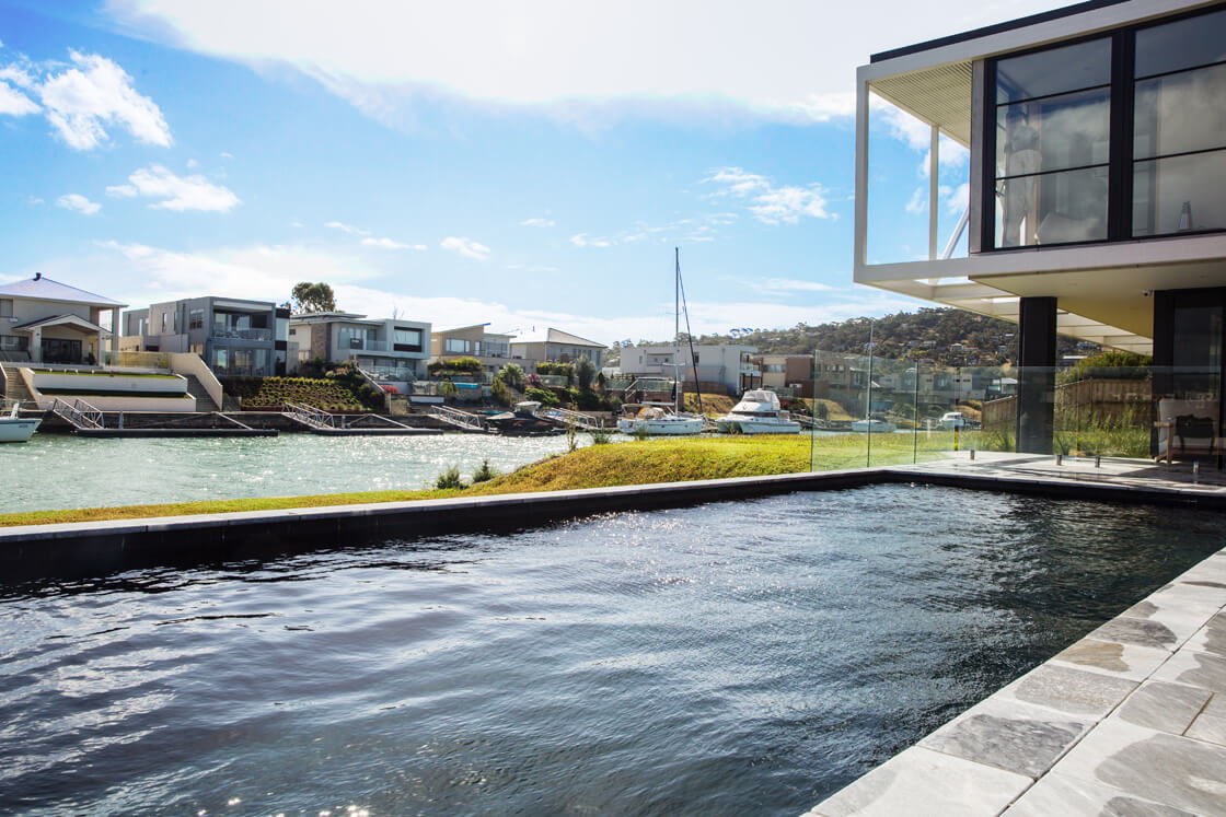 Infinity pool with waterfront views next to modern glass home