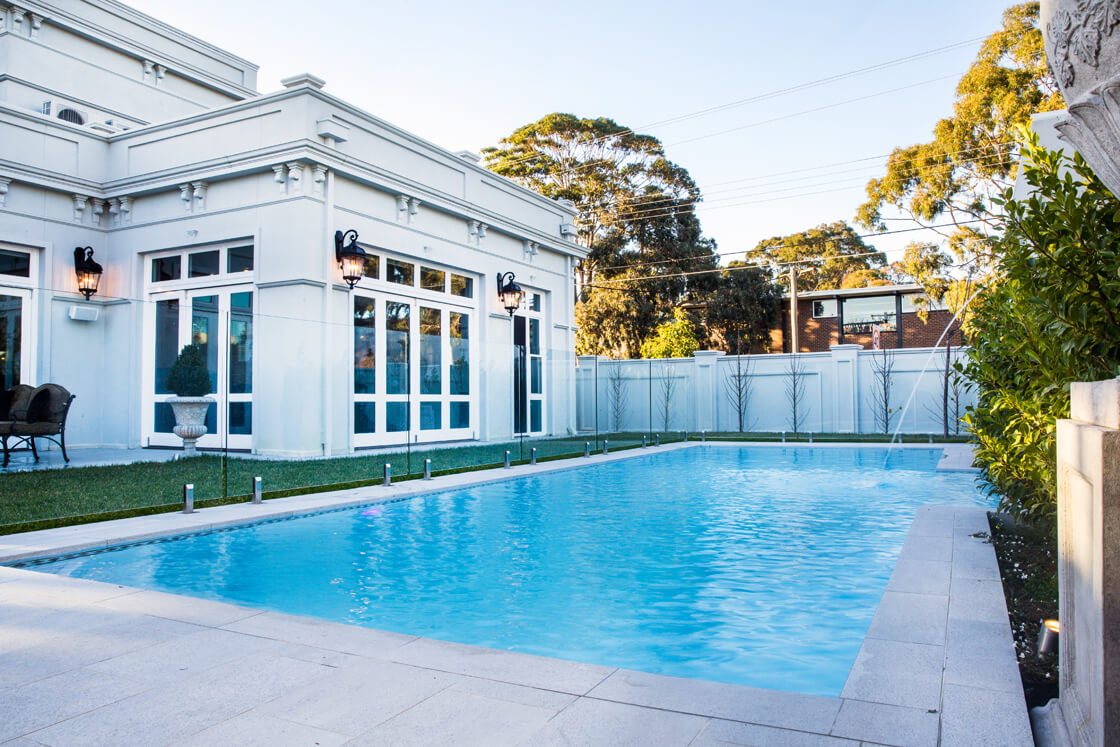 Expansive light blue pool outside white home with French doors and manicured lawn