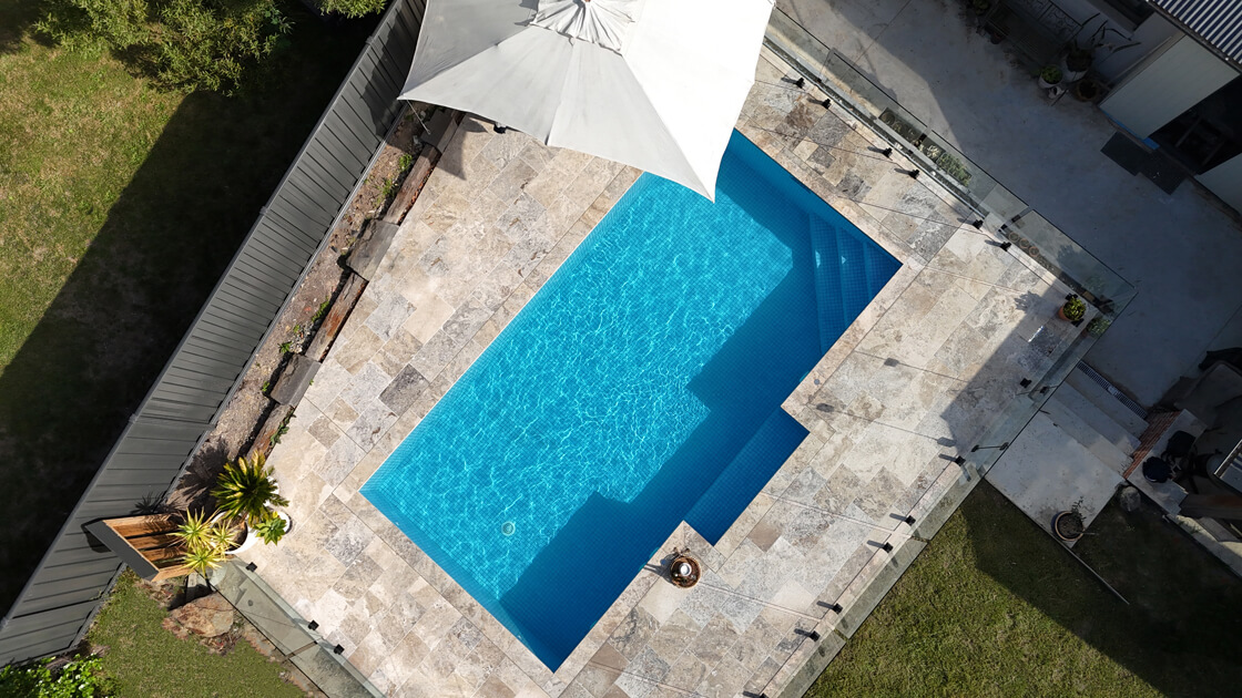 Aerial view of rectangular pool with natural stone paving and poolside umbrella