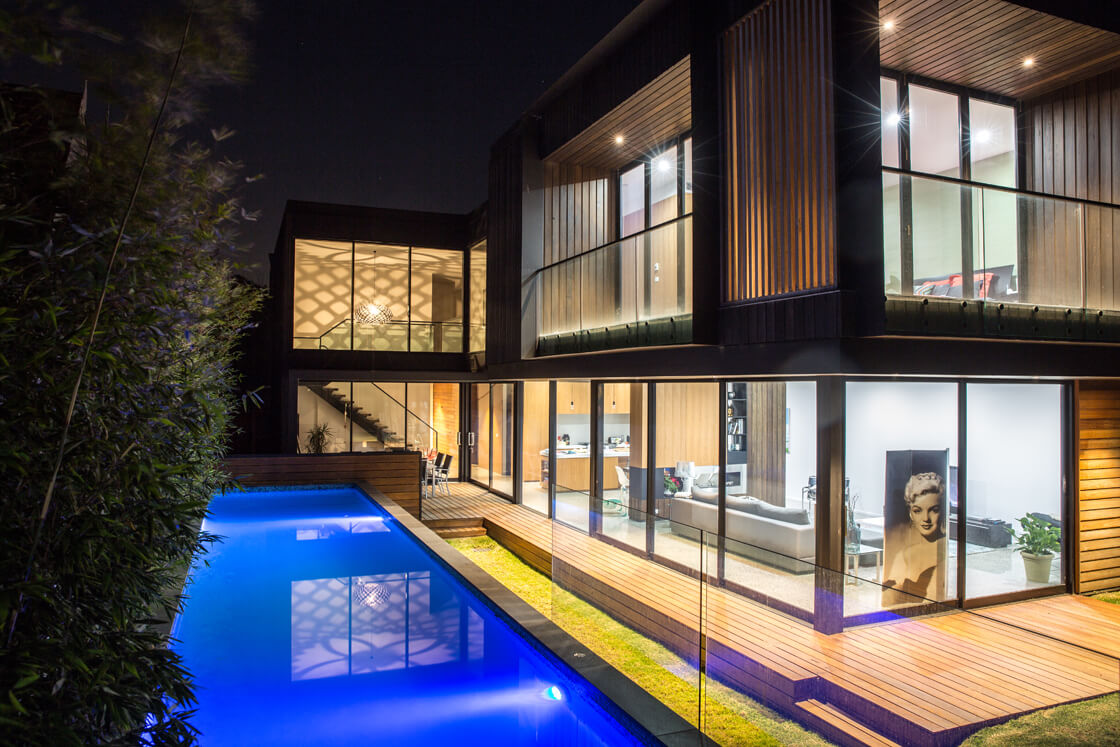 Night shot of lap pool next to luxury home with floor-to-ceiling windows