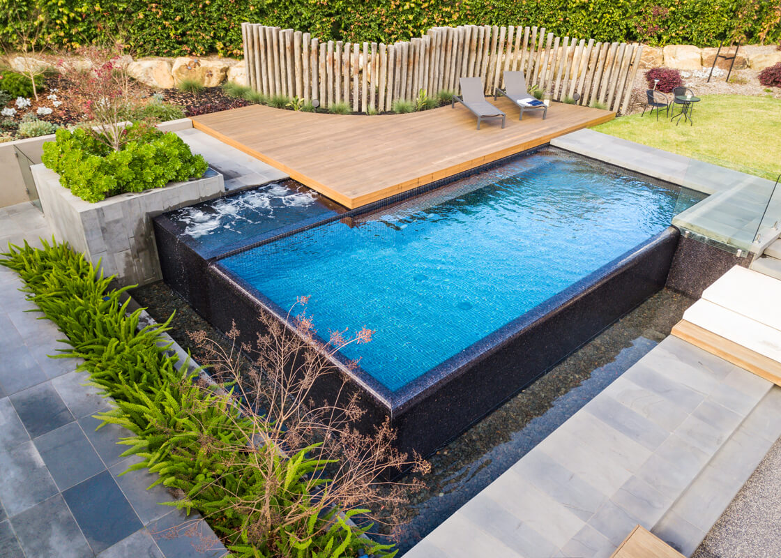 Infinity-edge garden pool surrounded by plants, decking and stone features