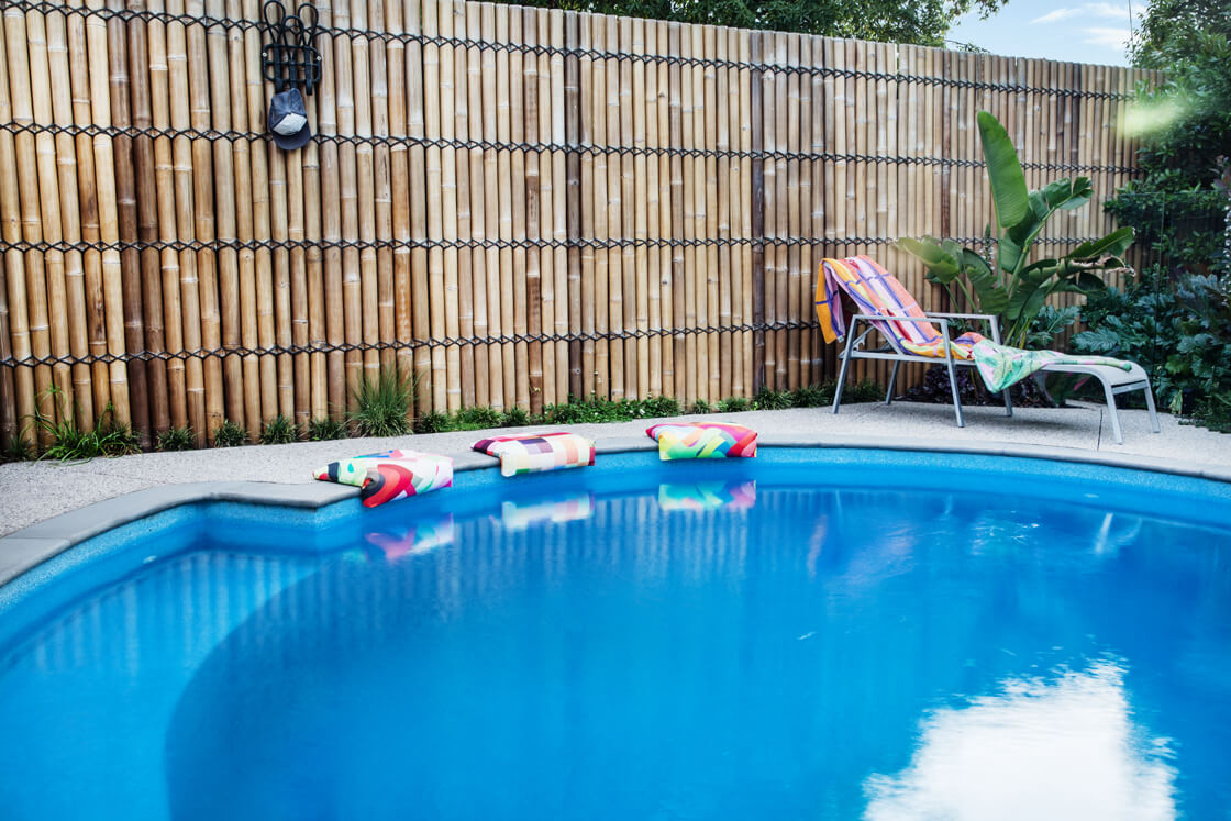 Curved pool with colourful cushions and bamboo fencing in tropical garden