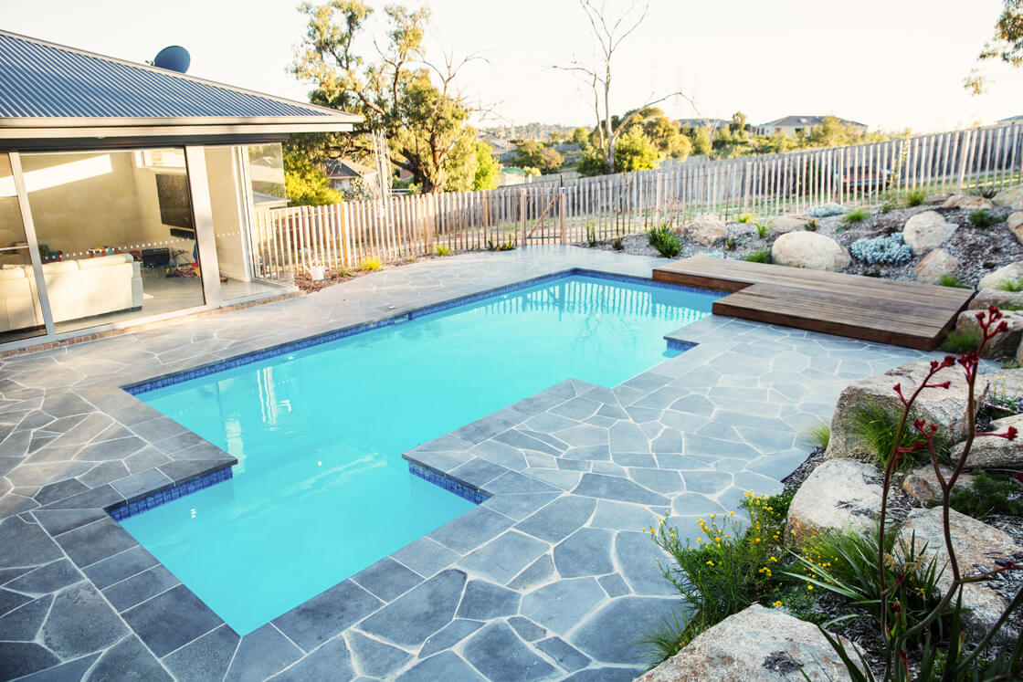 Natural pool with light blue water and flagstone paving in a native garden setting