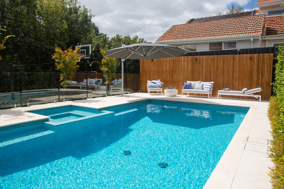 Family pool with spa and sports area surrounded by lounge chairs and timber fencing