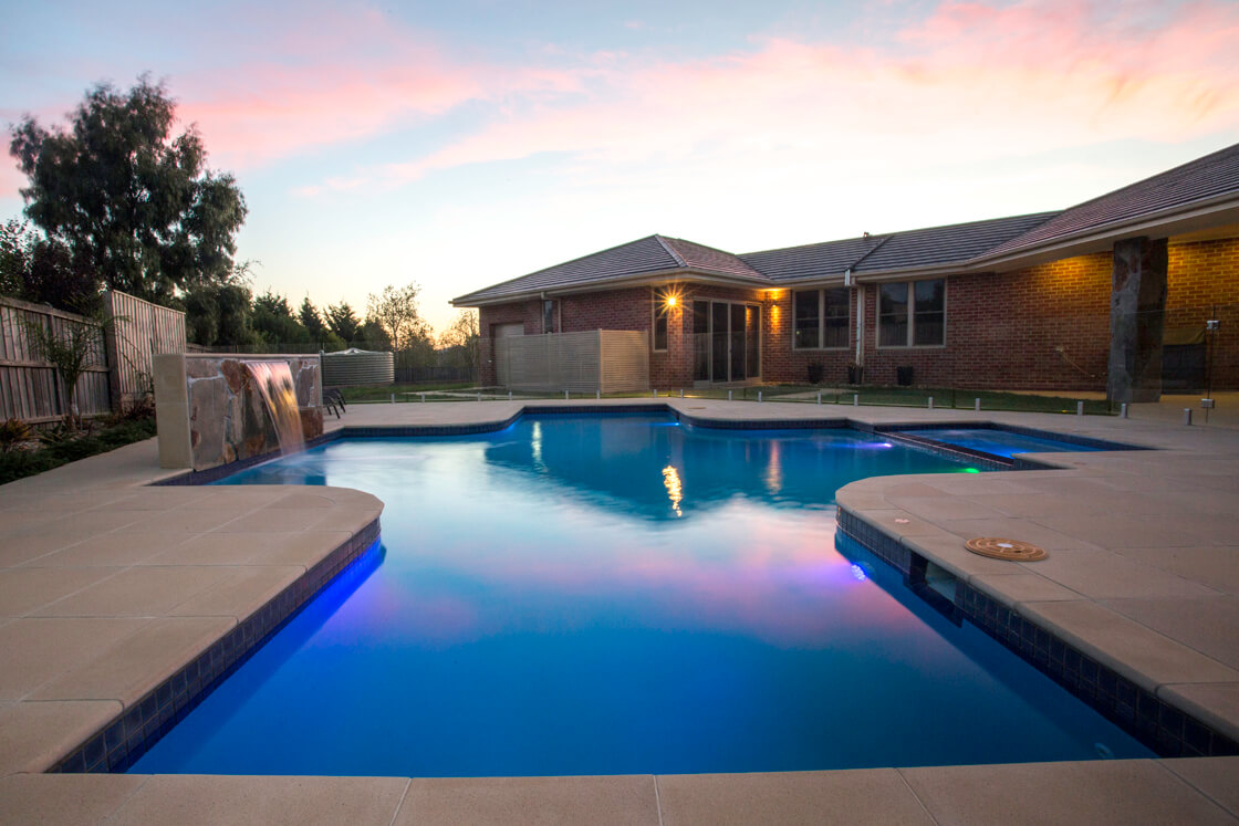 Twilight image of pool with feature waterfall and blue lighting