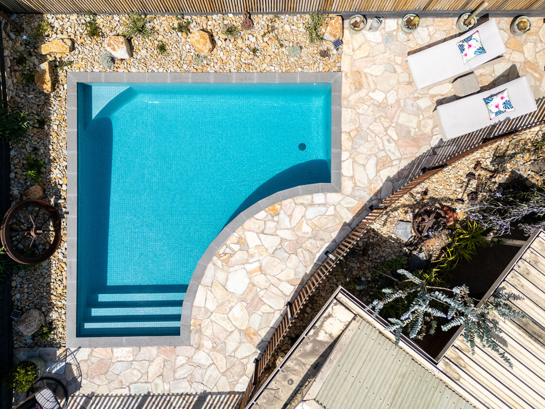Small curved pool with natural stone and pebbled landscaping