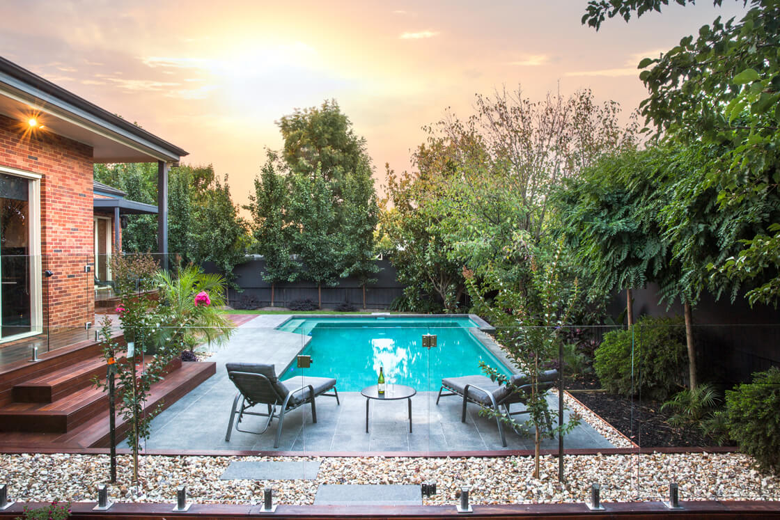 Backyard pool with tropical garden and sun loungers at sunset
