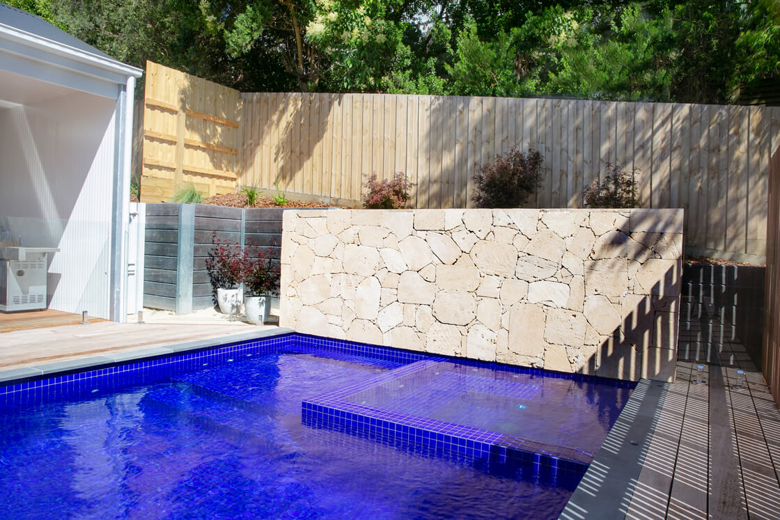 Bright blue tiled pool with limestone wall and timber accents