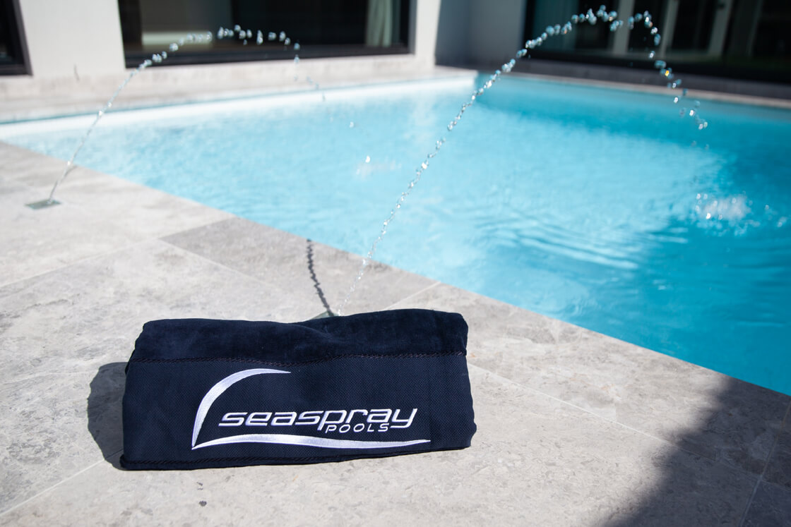 Seaspray towel on stone coping beside pale blue pool with fountains