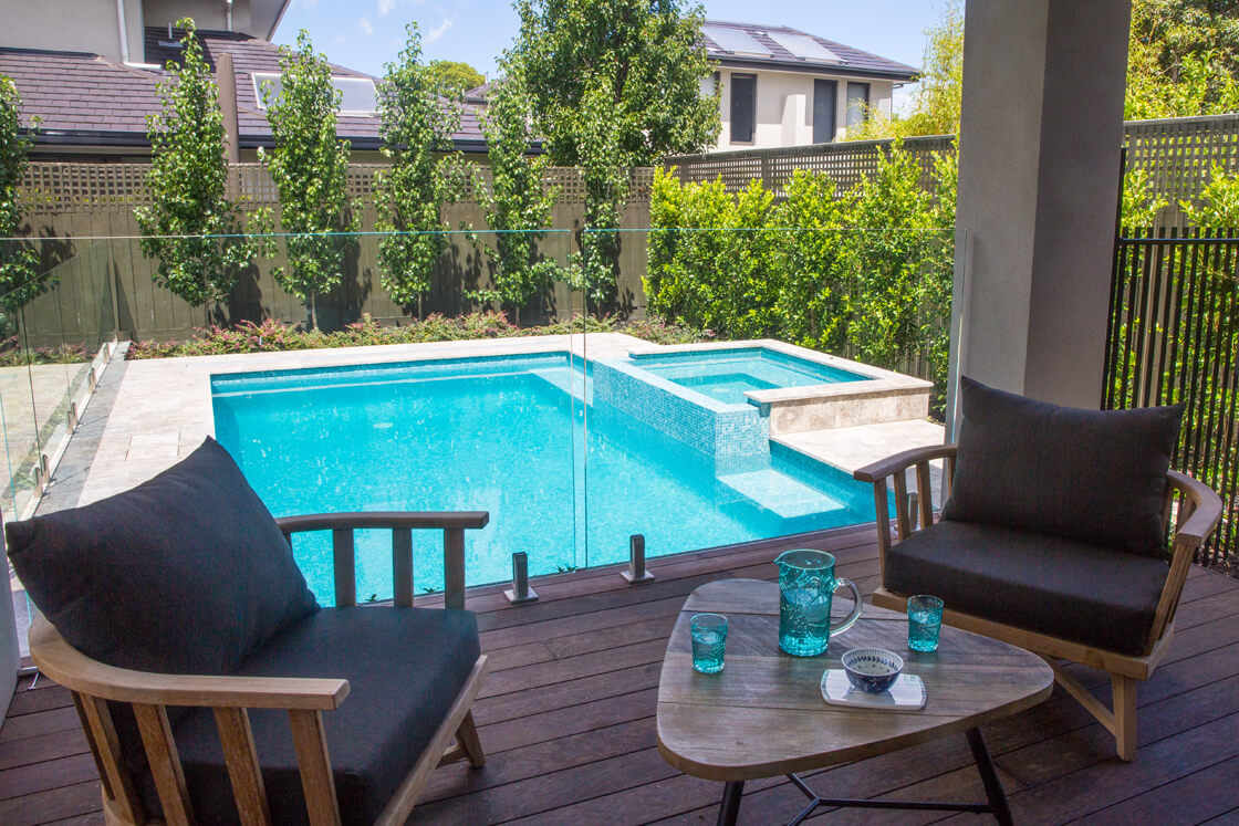 Courtyard pool with spa and seating area viewed through glass fence