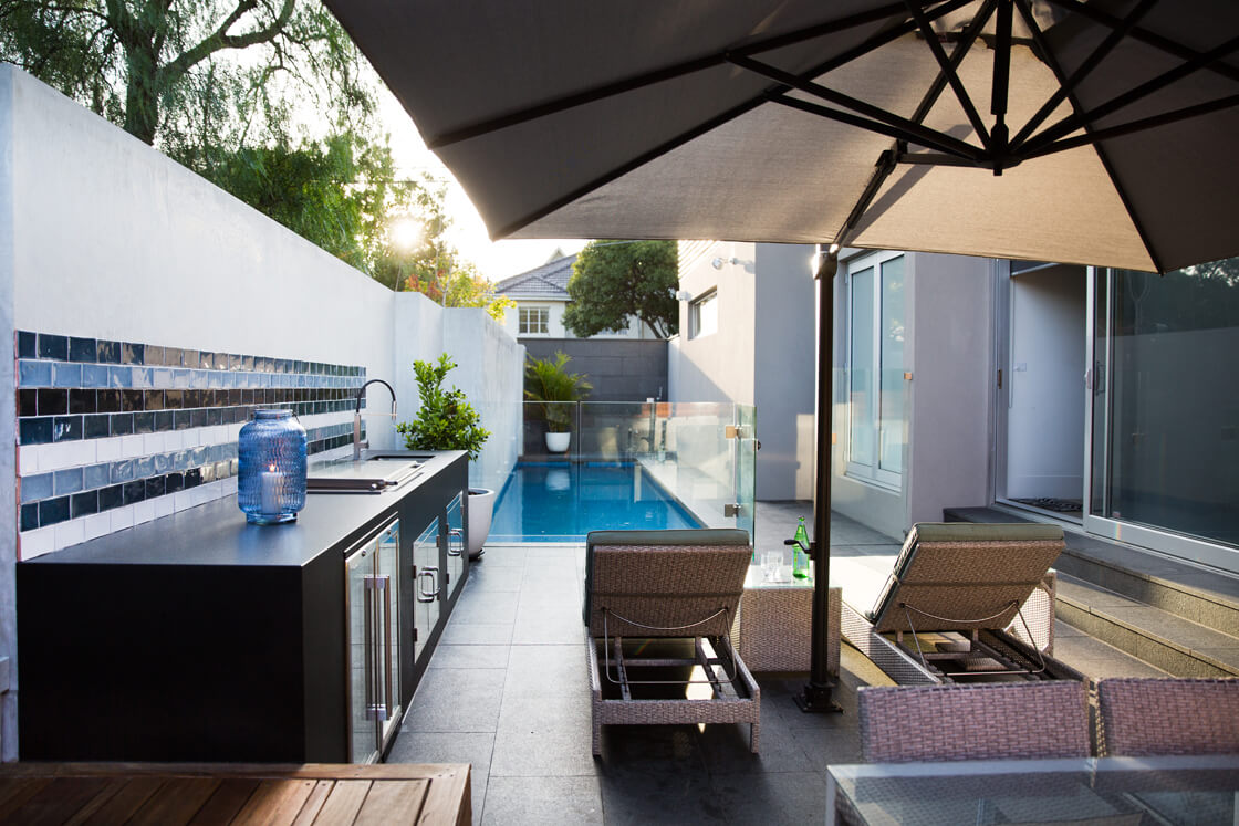 Modern plunge pool beside outdoor kitchen and sun lounges in narrow courtyard