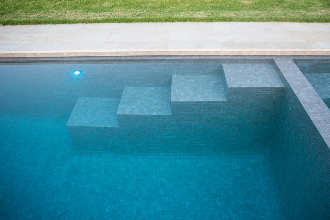 Close-up of large tile steps submerged in blue mosaic pool