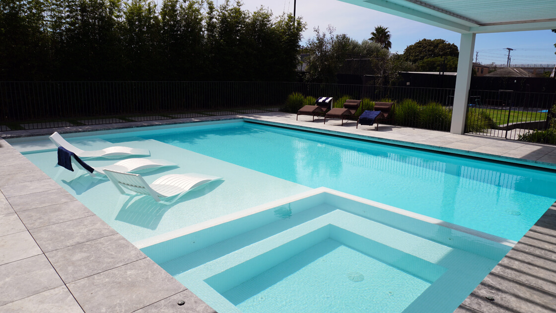 Light blue pool with in-water lounge chairs and spa in foreground