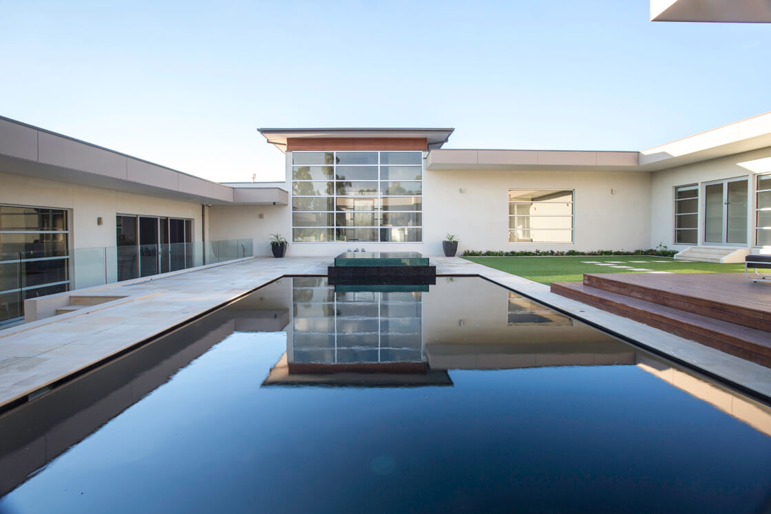 Black tiled reflection pool framed by white modern home