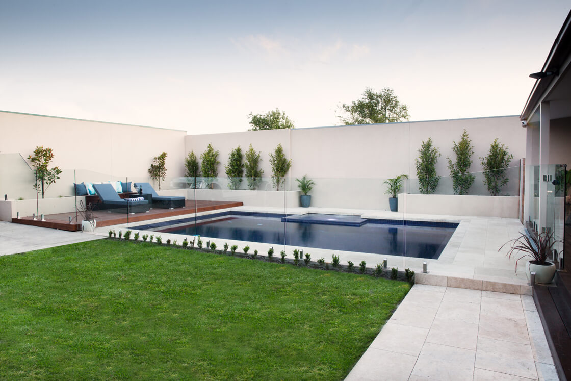 Contemporary backyard pool surrounded by lawn, deck and glass fencing