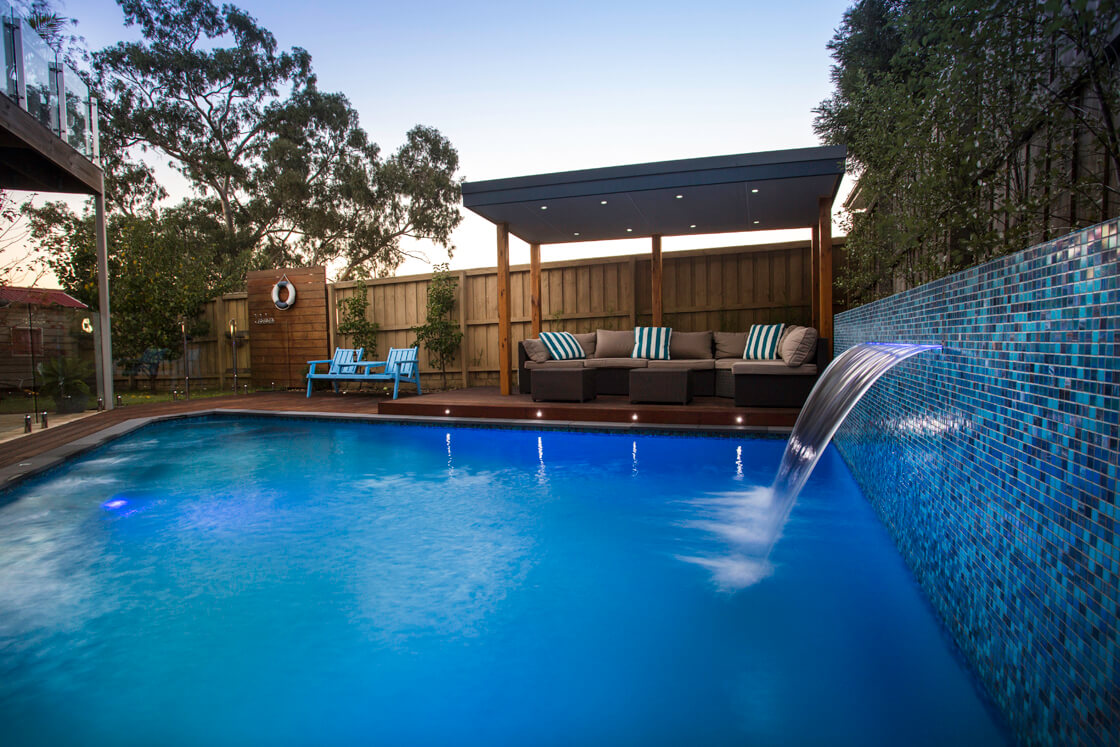Tiled pool with water feature and seating area at twilight