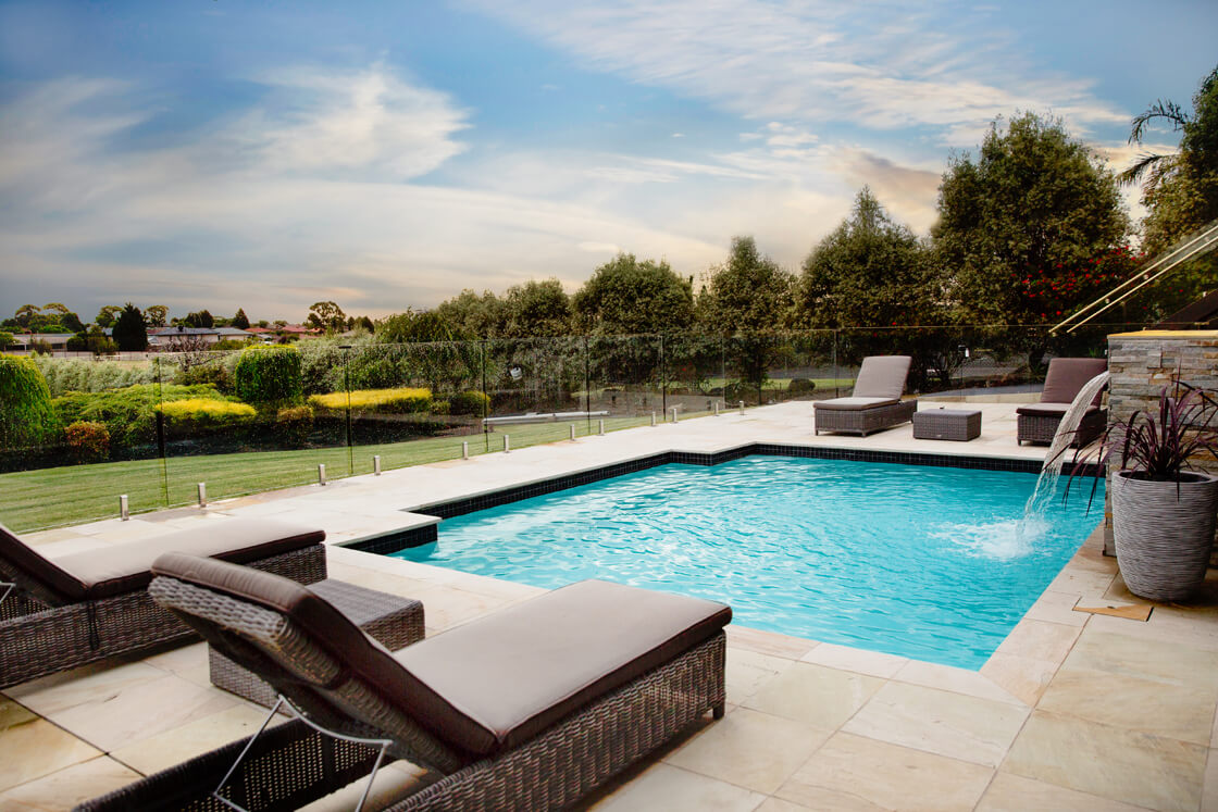 Rectangular pool with water feature and sun lounges in spacious landscaped garden
