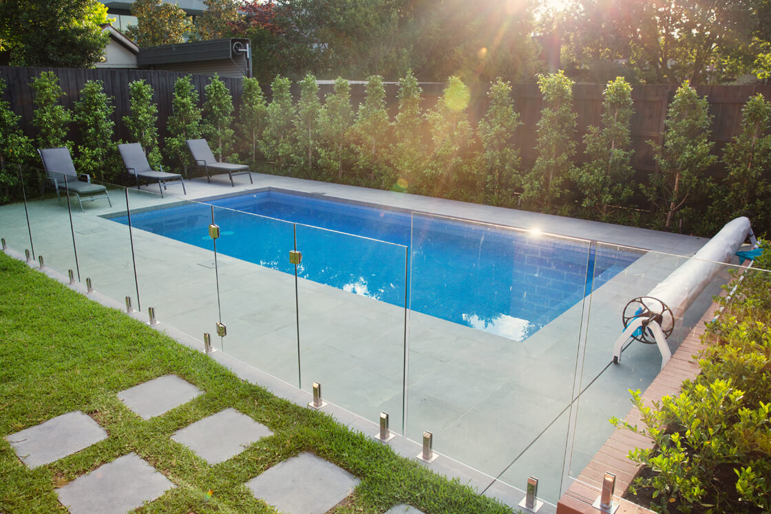 Rectangular pool with glass fence and sun loungers in landscaped yard