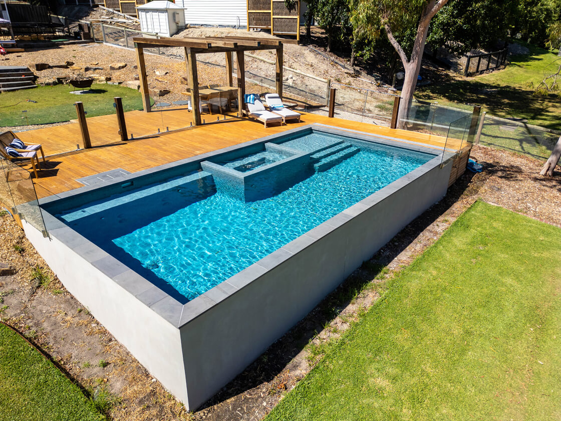 Raised concrete pool with glass fence and large timber deck
