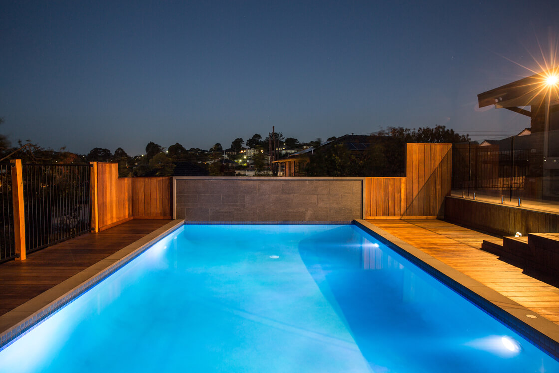 Modern rectangular pool at night with wood cladding and blue lighting