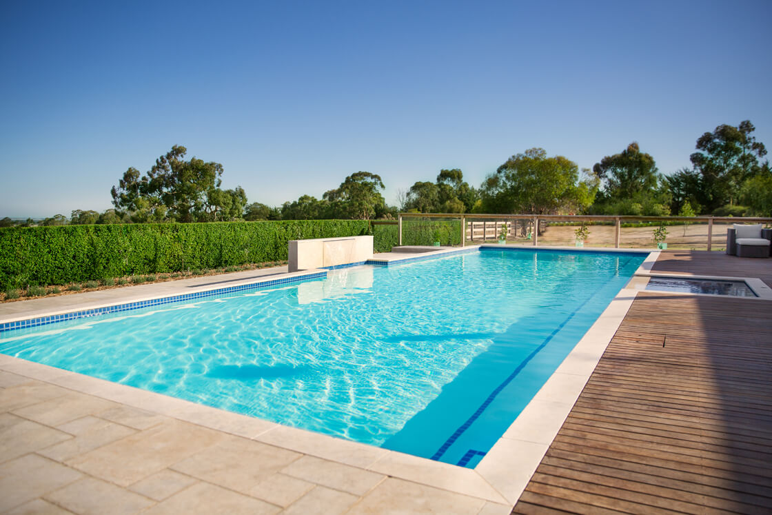 Lap pool in rural setting with hedges and pale stone tiles