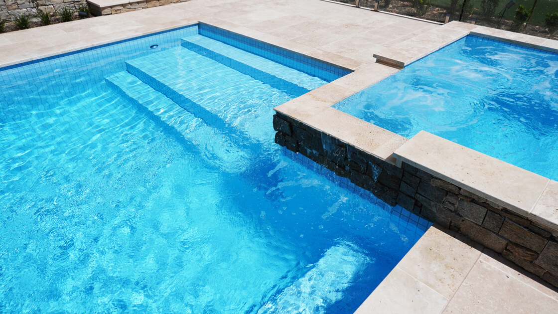Light blue tiled pool with raised spa and stone water feature wall