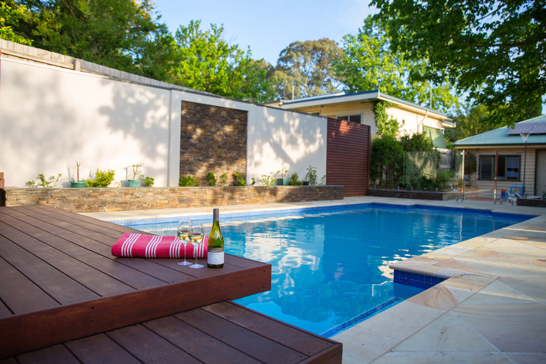 Backyard pool with raised timber deck, wine glasses and stone feature wall
