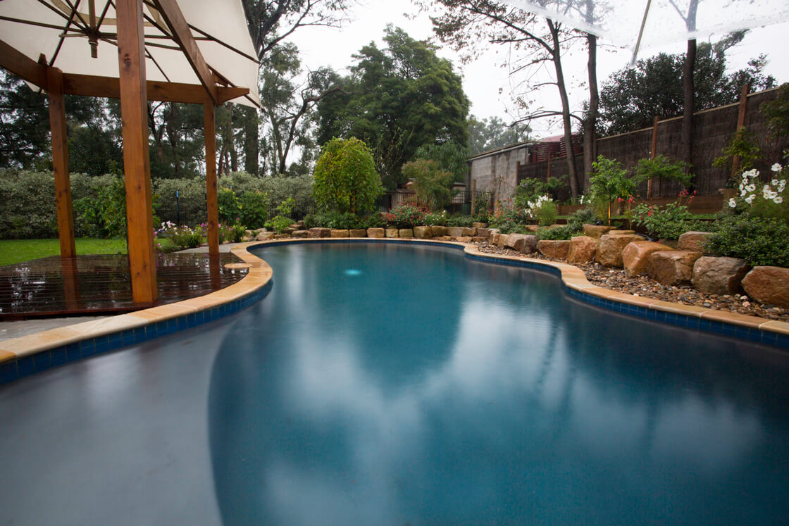 Freeform pool with stone edging, rustic garden and large umbrella