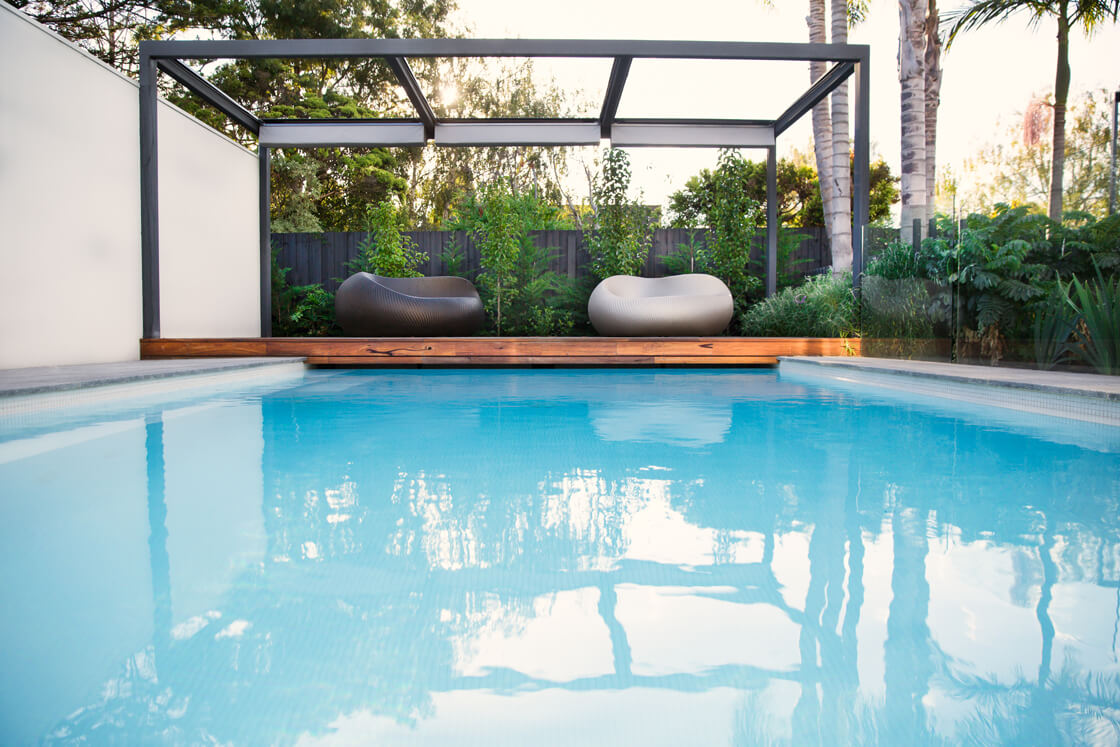 Light aqua pool with sculptural chairs under a metal-framed cabana
