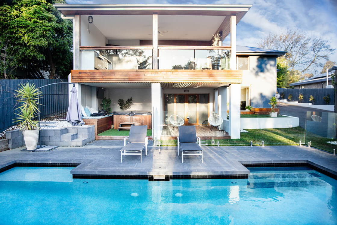 Large pool outside two-storey home with timber accents and alfresco zone