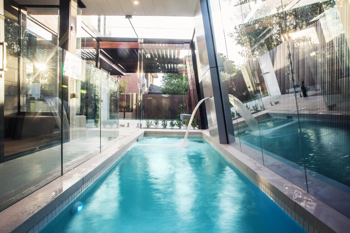 Indoor-outdoor lap pool with water spouts and floor-to-ceiling glass