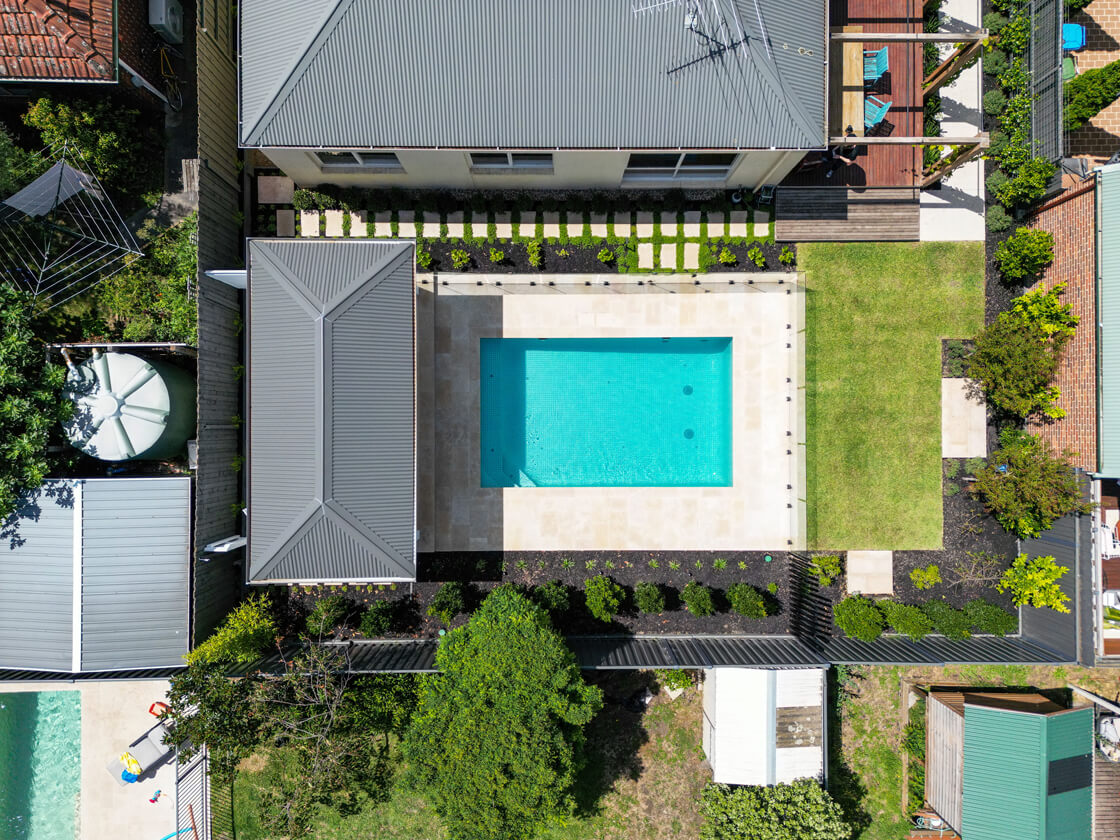 Aerial view of symmetrical courtyard pool with beige tiling and glass fence