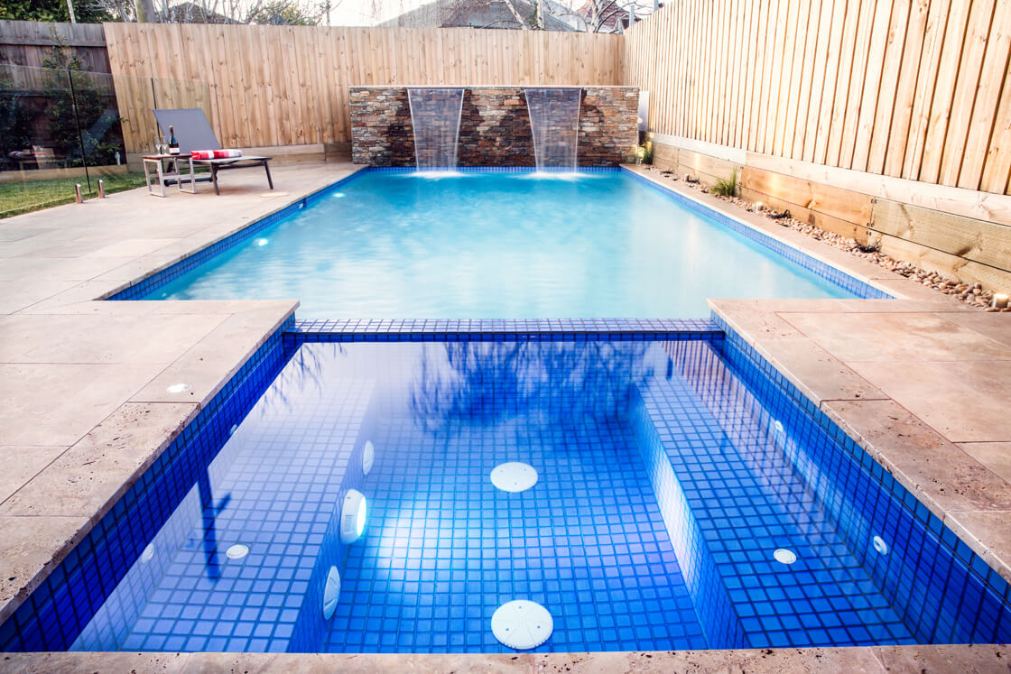 Bright blue tiled spa with attached pool and stone waterfall wall
