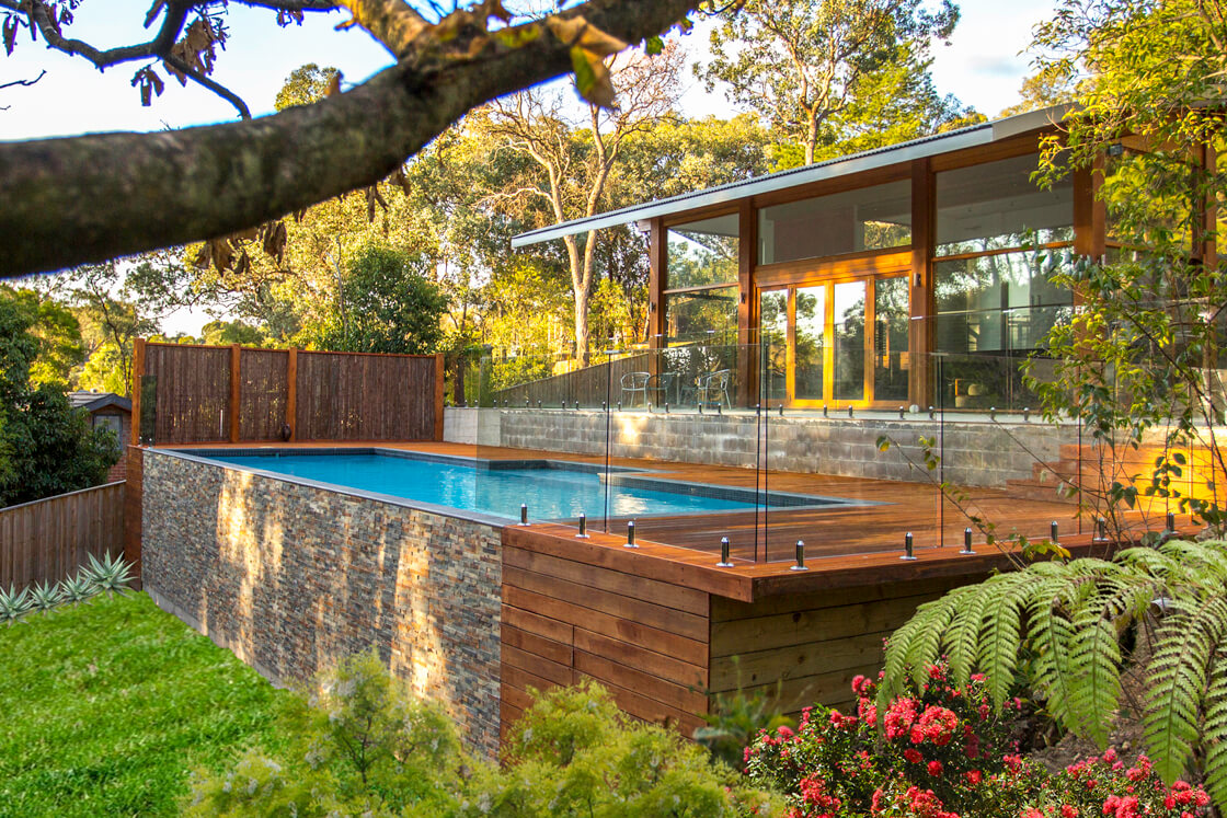 Above-ground pool with stone base, timber deck and forest backdrop