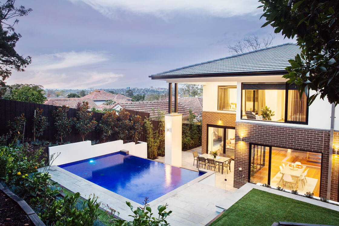 Blue tiled pool at sunset with garden and city views from elevated courtyard