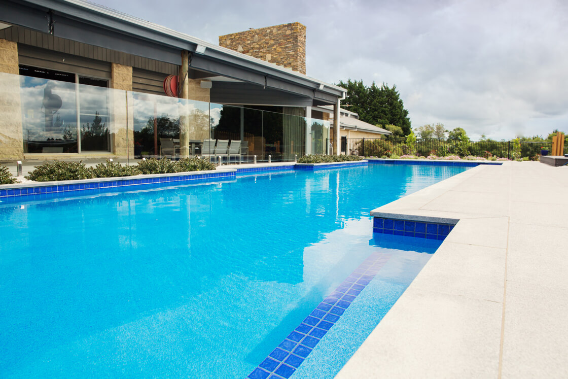 Blue tiled pool with expansive surrounds and feature stone walls