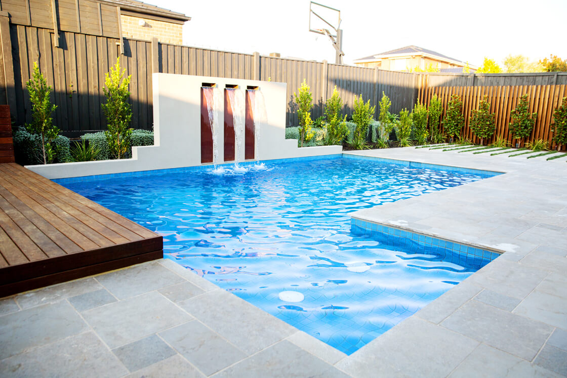 Backyard pool with water wall and vertical feature panels beside wooden deck