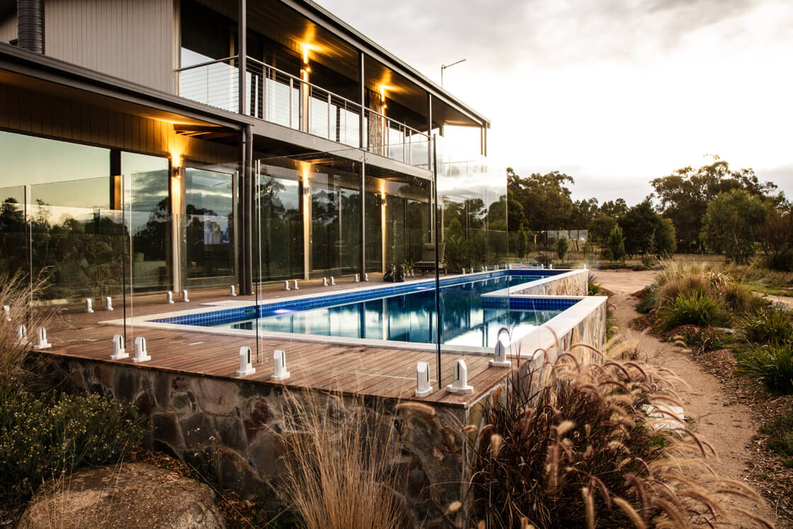 Glass-fenced pool on bush block with large home and timber elements