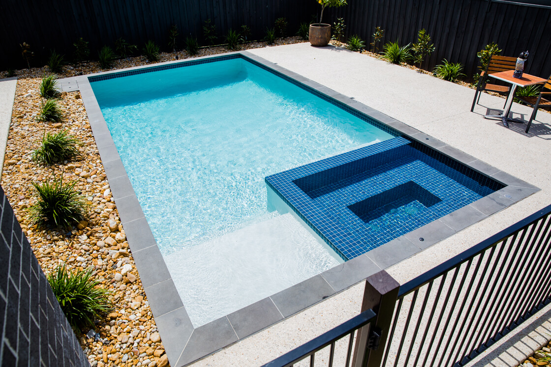 Compact backyard pool with elevated spa and pebble landscaping