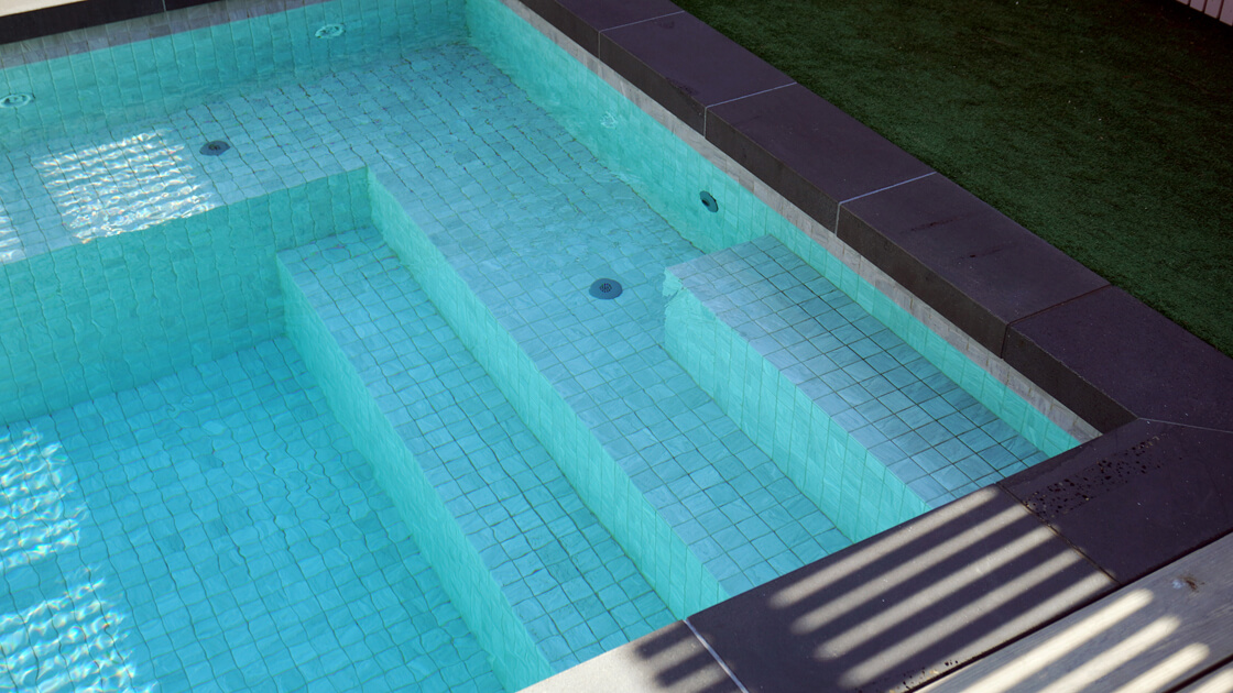 Aqua tiled pool steps with sunlight reflections and clean edge detail