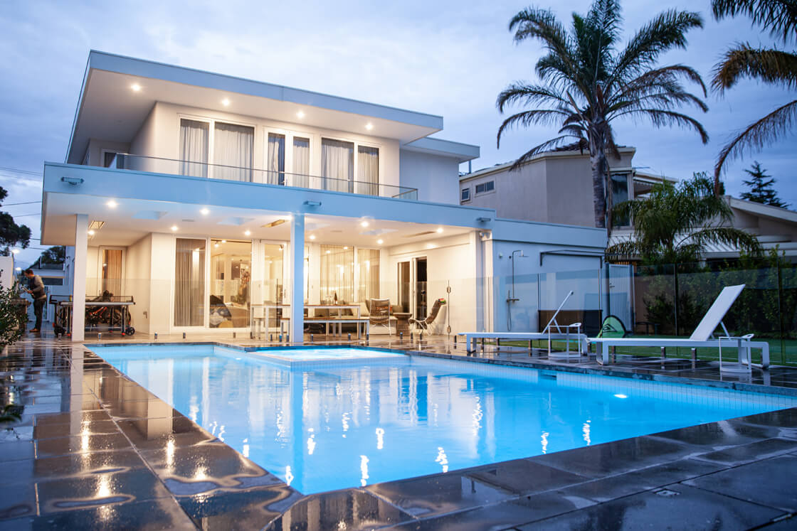 Twilight image of home and pool with glowing glass fence and alfresco
