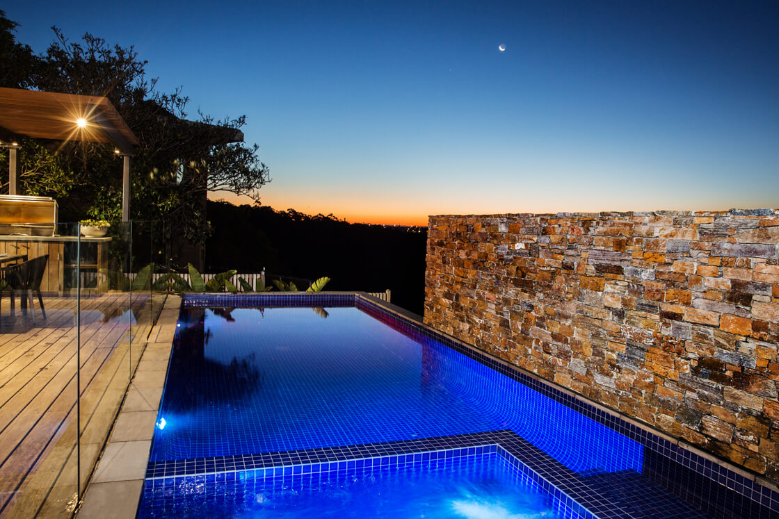 Infinity edge pool at sunset with stone wall and timber deck