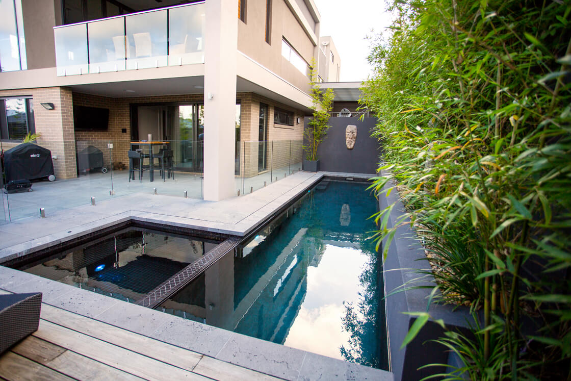 Dark-tiled lap pool with glass fencing and bamboo screening