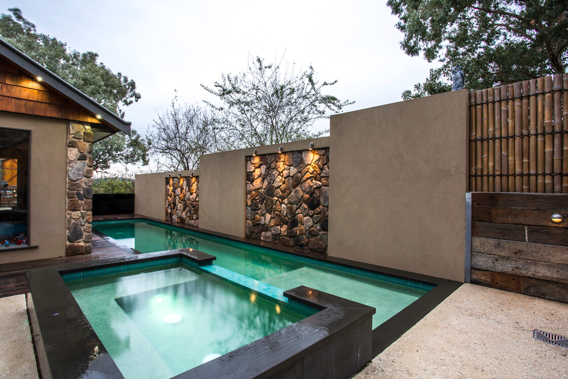 Green-blue tiled pool and spa with uplights and stone wall features