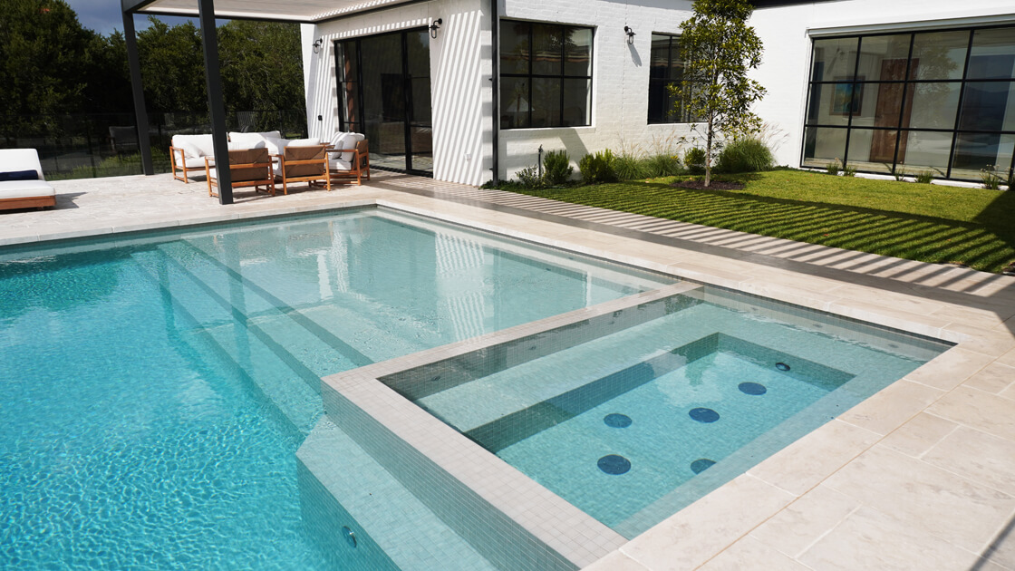 Pale tiled pool with white coping, black-framed doors and clean outdoor furniture