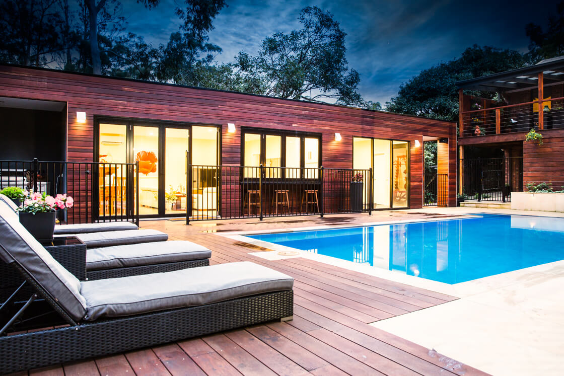 Backyard pool with timber feature wall and lounges on deck at night