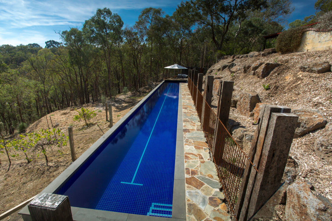Long lap pool with bush views, blue tiling and stone path edge