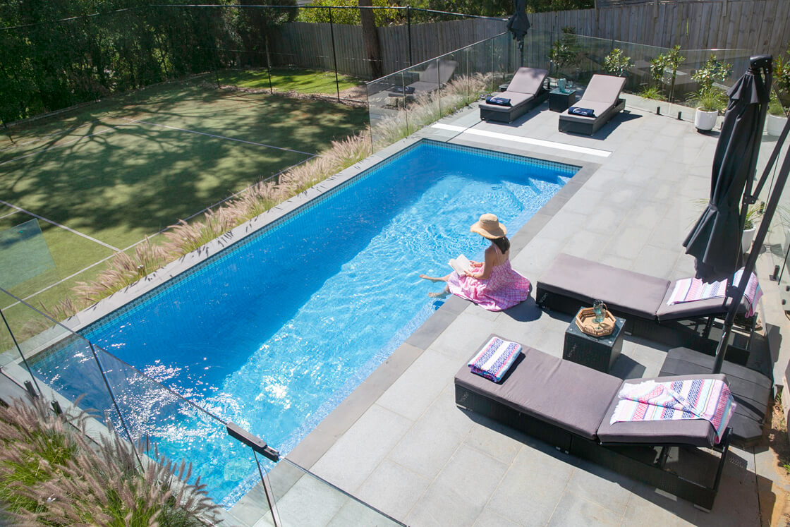 Small lap pool next to tennis court with lounging area and privacy fencing